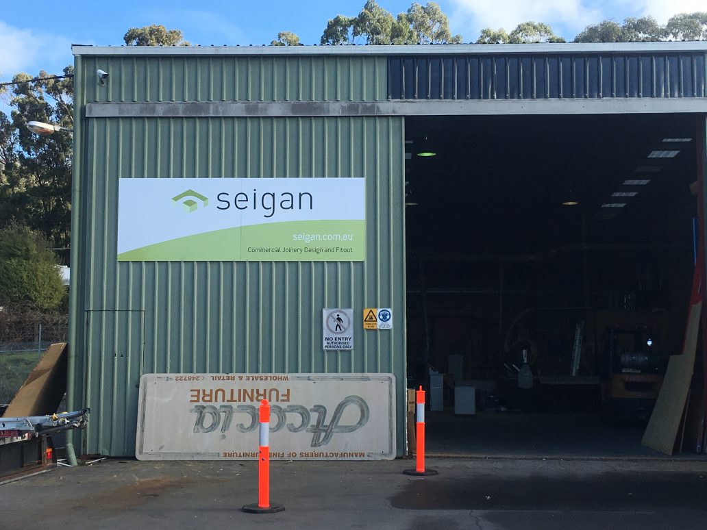 Wall-mounted Seigan ACM panel sign on a green warehouse exterior